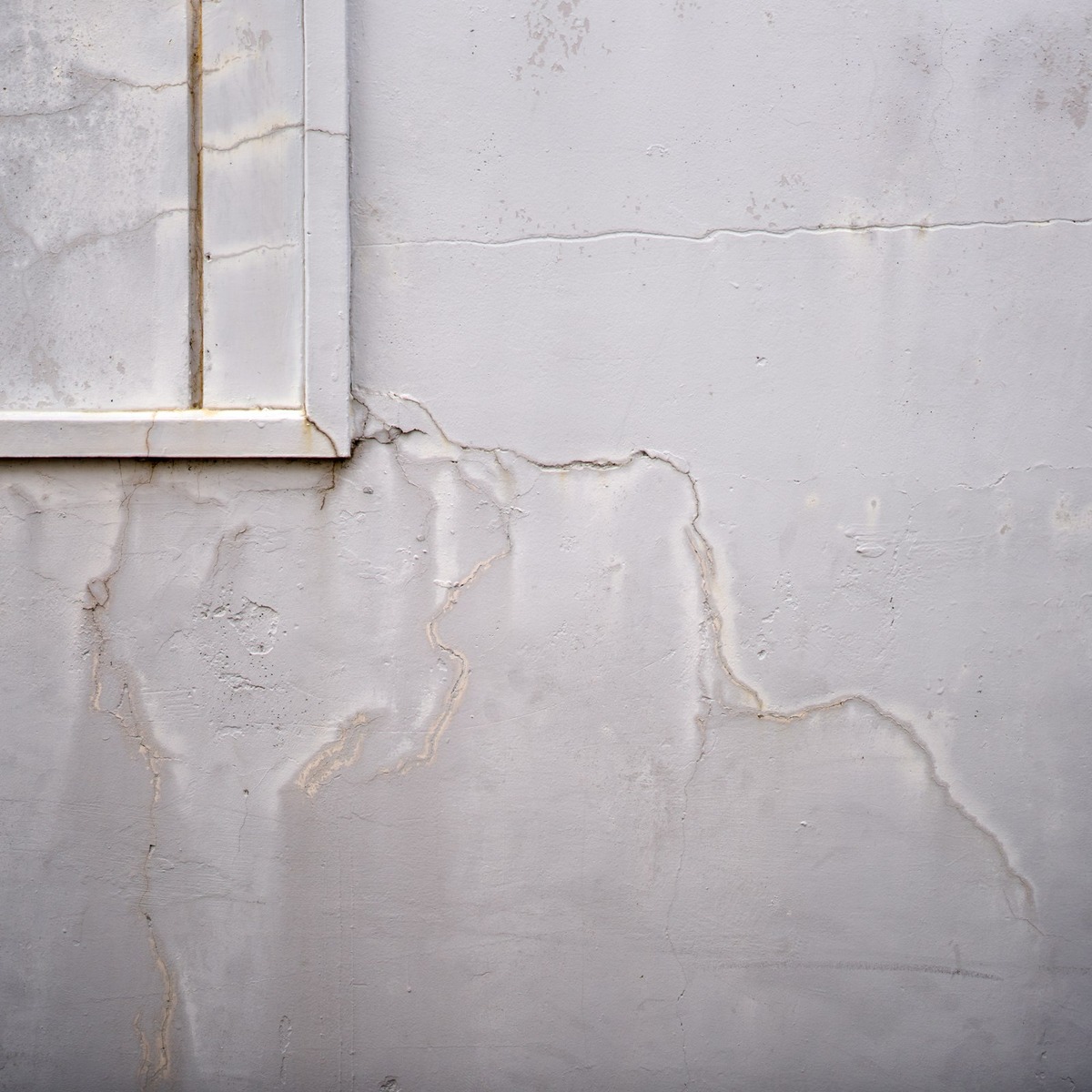 Close-up of multiple cracks spreading across a concrete foundation wall near a window, showing visible damage requiring expert foundation repair in Palm Beach Gardens, FL.