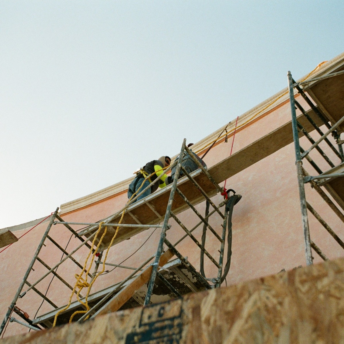 Construction workers on scaffolding performing exterior structural work on a building, representing expert foundation repair services near me.